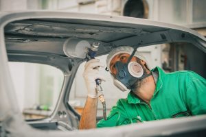 Operator wearing a respirator works on grit blasting a car's frame