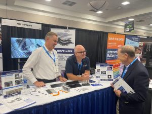 two laser sales men talk to a customer at a tradeshow for battery applications