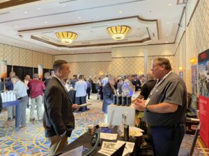 A nuclear sales manager for laser cleaning systems speaks to a potential customer on a tradeshow floor in a hotel ballroom