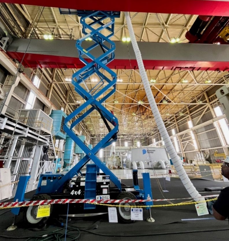 A blue scissor lift is extended up towards the ceiling of a turbine building